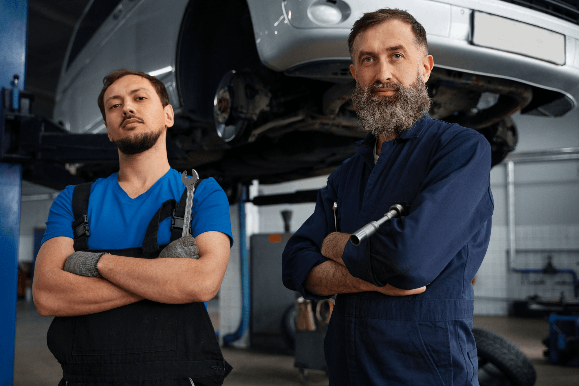 Automotive mechanics in garage workshop standing before vehicle on hydraulic lift