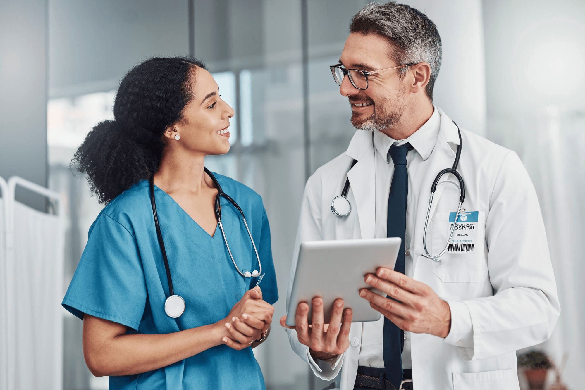 Registered nurse in scrubs and physician in white coat consulting patient charts on a digital tablet